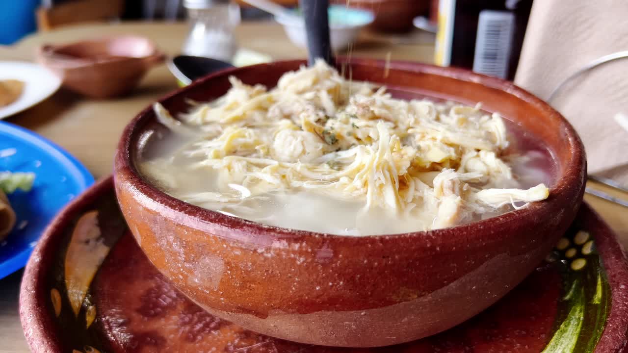 Hands adding ingredients to a bowl of white pozole, mexican food