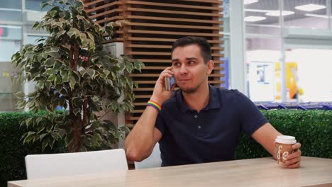 joven con simbolismo arco iris en un café, hablando por teléfono y sonriendo