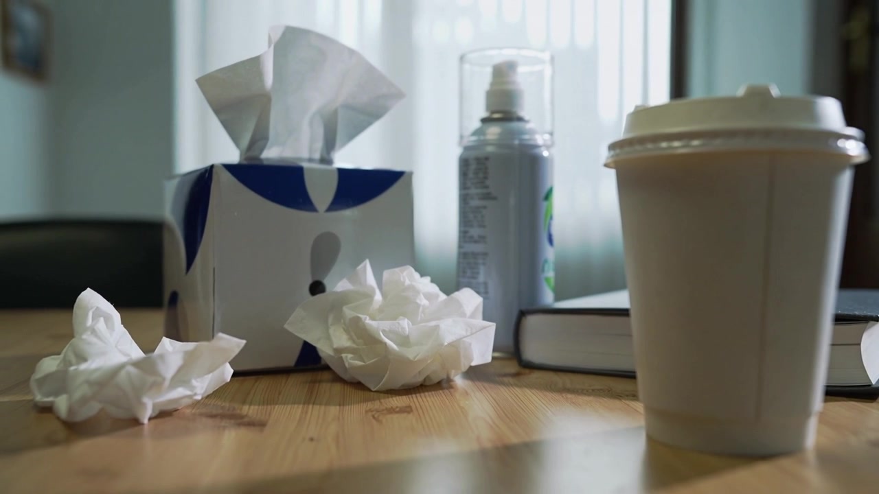 Shifting camera revealing blue tissue box and crumpled tissues on wooden table, emphasizing details