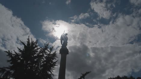 timelapse of sun-moon passing behind cemetary statue on pillar