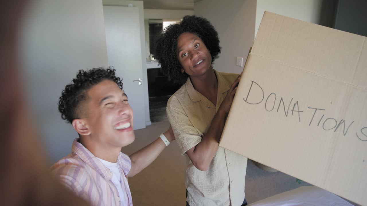 Uomini afroamericani che salutano sulla soglia della camera da letto, con la fotocamera selfie che inquadra e mostra una scatola per DONAZIONI.