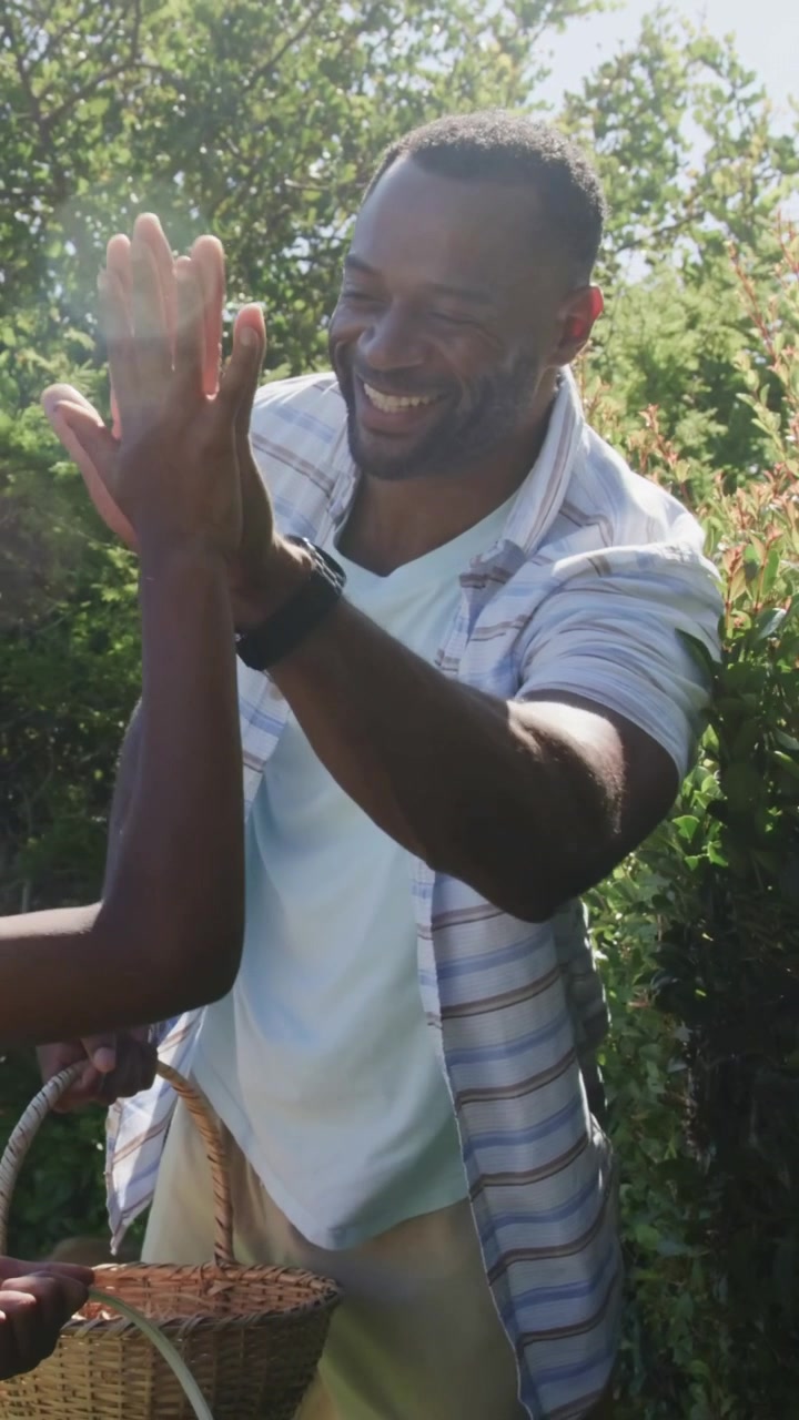 Video verticale: Papà che alza la mano e porta il figlio a darsi il cinque in giardino per festeggiare, con cestino di vimini e orologio.