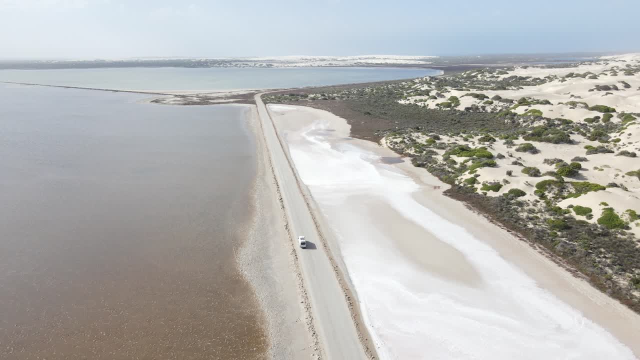 drone aéreo sobre campervan blanco conduciendo en la carretera sobre el lago rosa macdonnell y las dunas de arena boscosas en el sur de australia