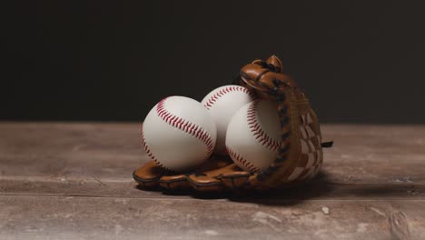 baseball still life with person picking up ball from catchers mitt on wooden floor