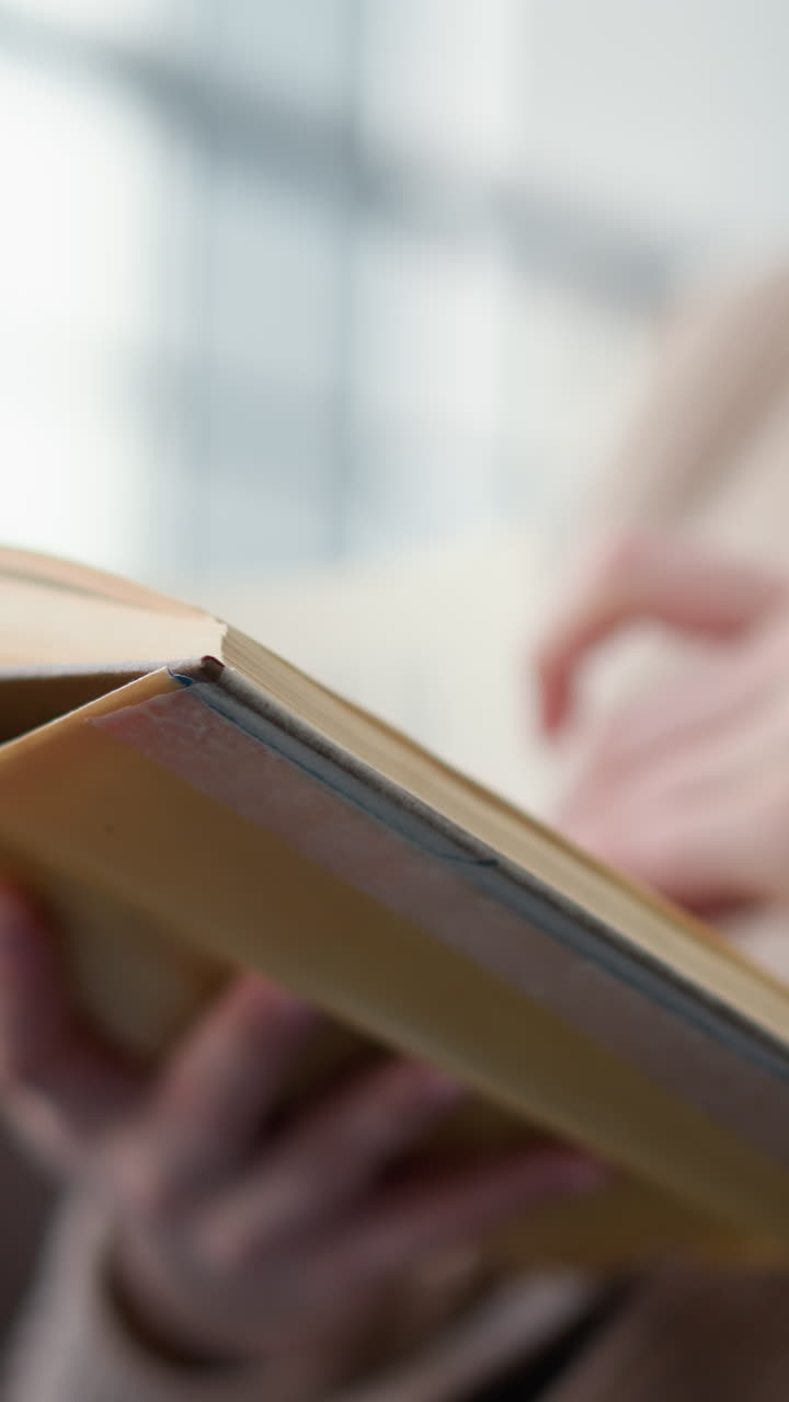 primer plano de una joven que sostiene un libro mientras lee atentamente en un ambiente acogedor y relajado, sus dedos pasan suavemente por las páginas mientras se sumerge en la lectura