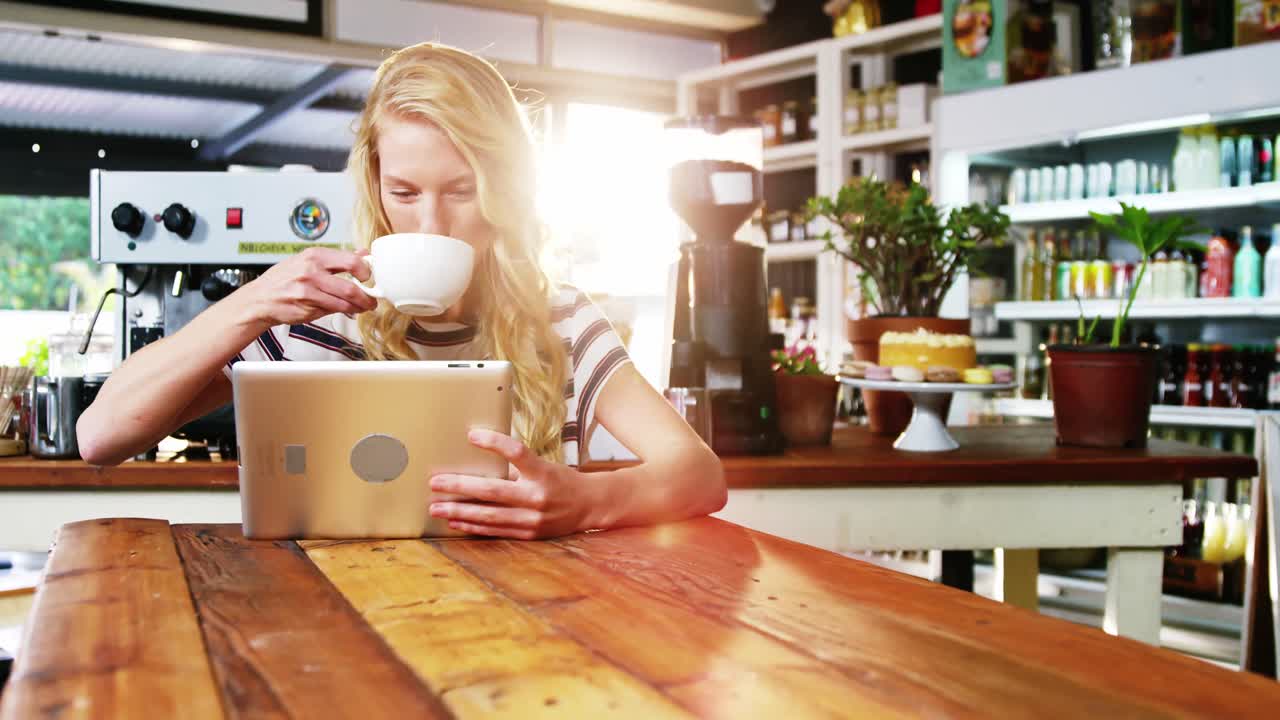 mujer usando una tableta digital mientras toma una taza de café