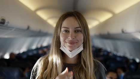 retrato de una mujer de pie en una fila de asientos en un avión, quitándose la máscara para sonreír