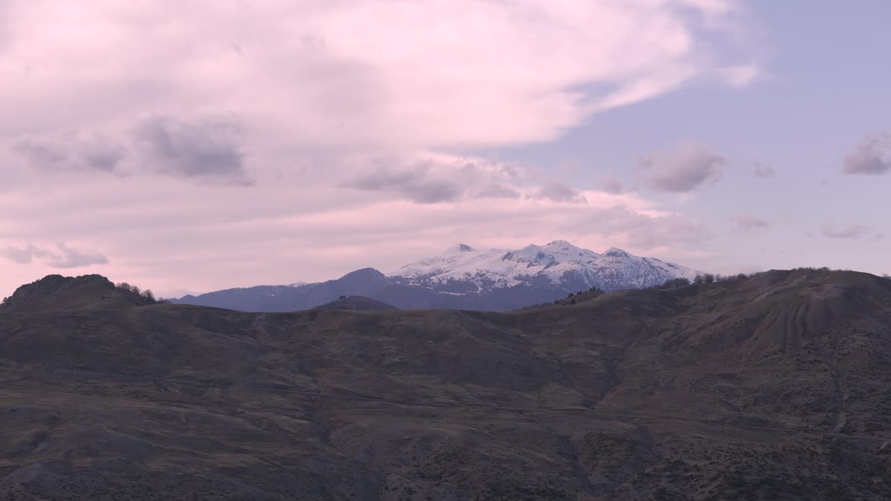During sunrise drone flies over rocks, revealing snowy mountains in the distance