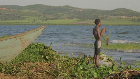 a young african boy stands on the shores of lake victoria and looking out into the distance.