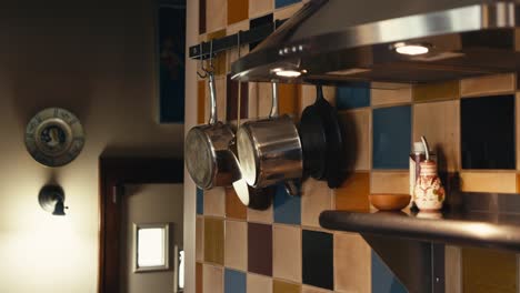 pots and pans hanging on hooks inside of a kitchen next to a stove with a colorful backsplash