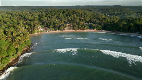 establishing aerial drone shot of hiriketiya beach and bay with surfers in water and waves breaking in tropical sri lanka south coast