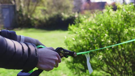 close up side view of man struggling to feed slack line through ratchet outside