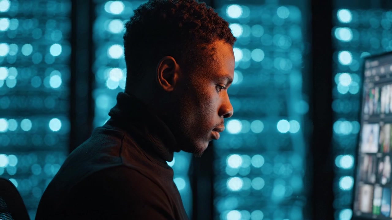 Focused individual at a computer, deep in thought, illuminated by glowing blue lights in a modern technology-driven environment, enhancing the atmosphere of innovation.