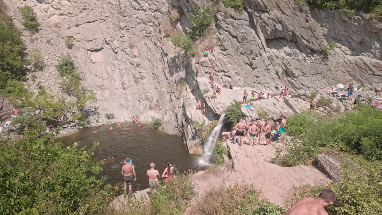 Crowds of people enjoying a sunny day at a waterfall cliff jumping spot