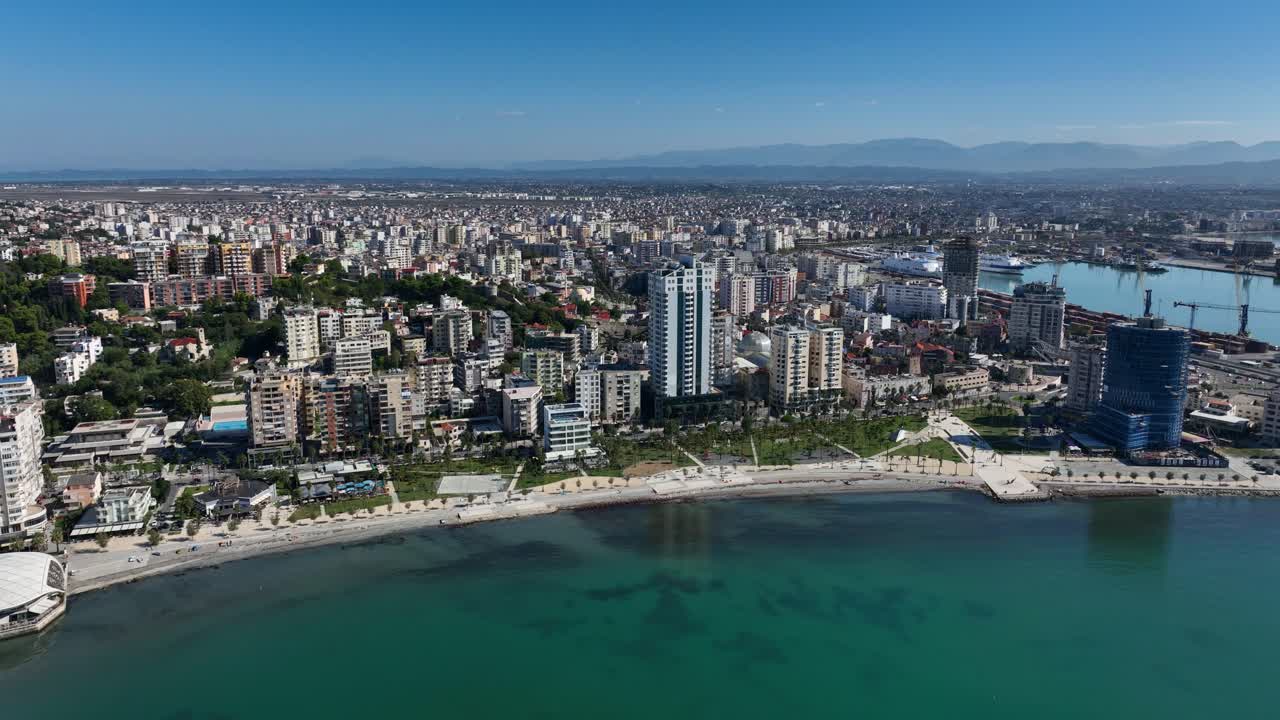 Durres beachfront with buildings and clear turquoise water on a sunny day in Albania, panoramic aerial orbit establishing