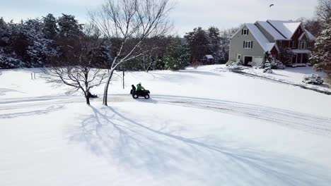 A-low-angle,-panning---tracking,-aerial,-drone,-birds-eye-view-of-a-four-wheeler-quad-driving-in-the-winter-snow-with-a-child-on-the-back-while-pulling-a-sled-with-an-excited-child-enjoying-the-ride