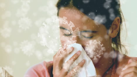 animation of macro covid-19 cells floating over biracial woman sneezing into a tissue