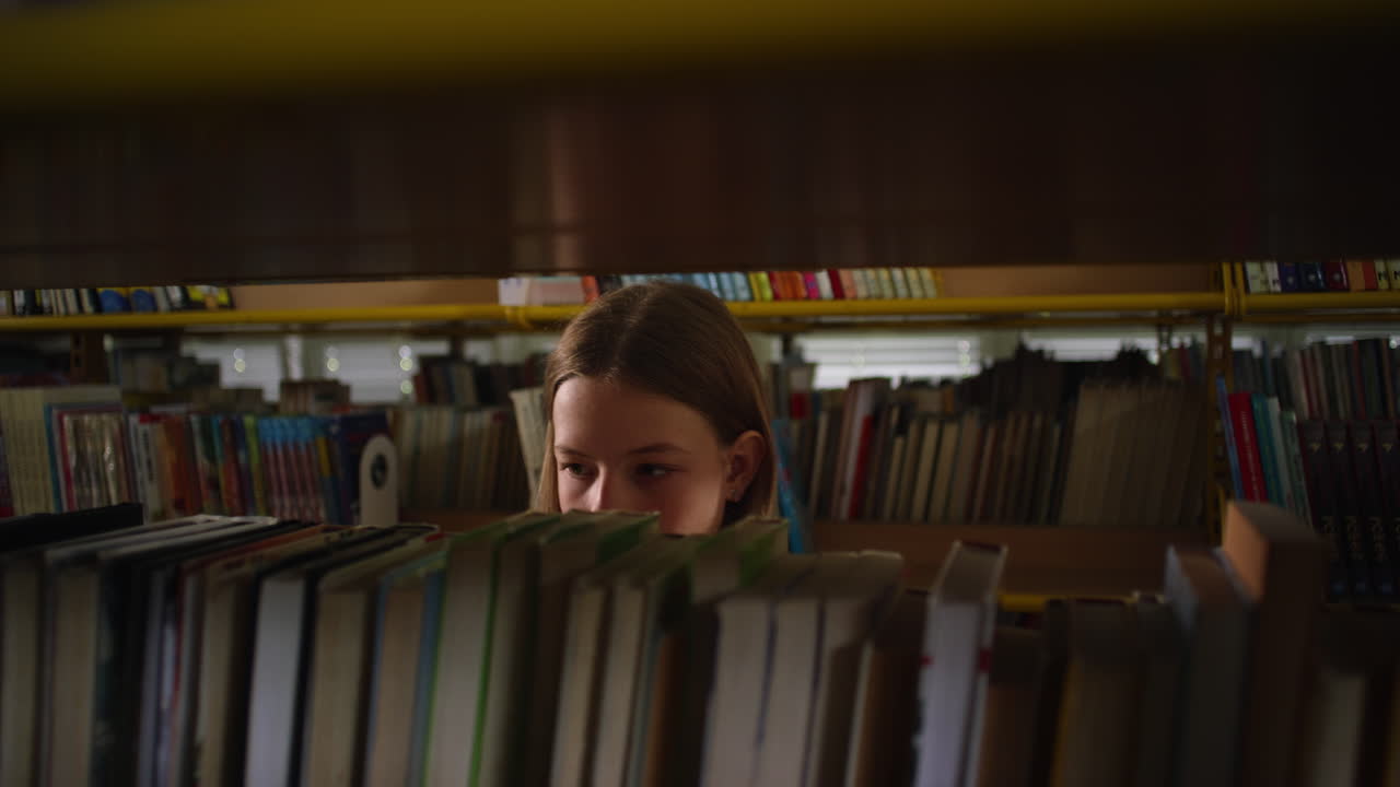 vista de una niña a través de las estanterías de la biblioteca, buscando un libro, disparo de mano