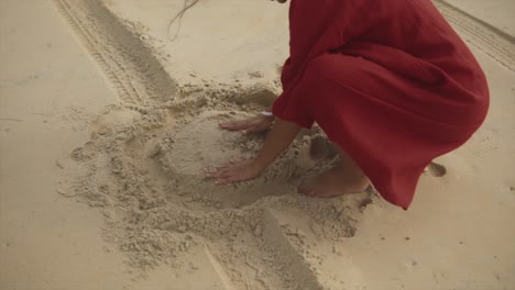 ad adult girl in a red dress playing with sand on a beach with bare feet