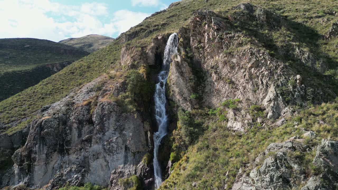 Aerial ascends mountain slope to Caryacuyo Waterfall in southern Peru