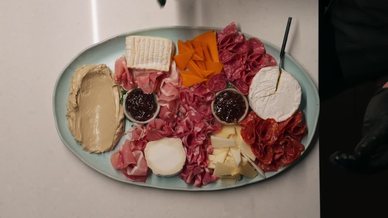 Papan charcuterie yang semarak disiapkan dan diisi dengan berbagai keju dan daging olahan (gerak lambat, 4K).