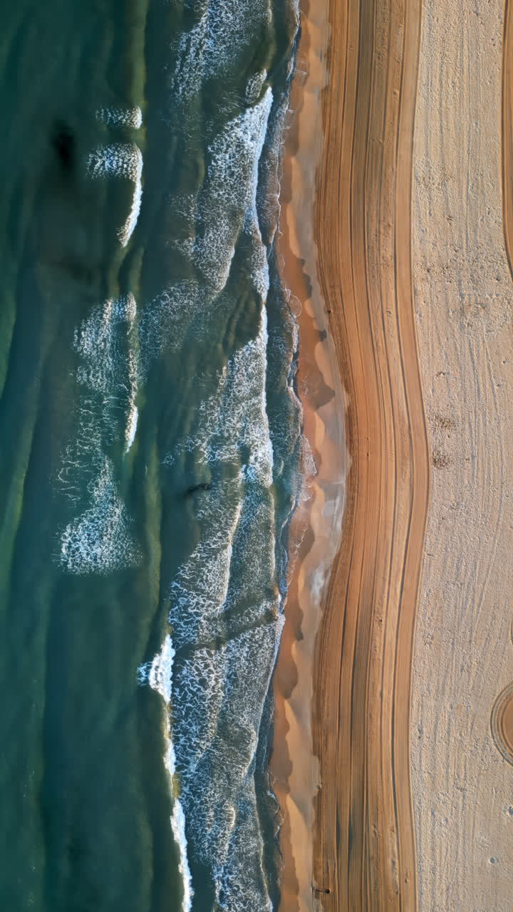 Vista aerea da drone delle onde che si infrangono sulla riva della spiaggia di Alicante, Spagna. Verticale