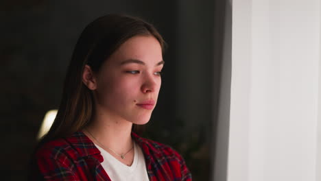 pensive long haired young woman looks out of window in room