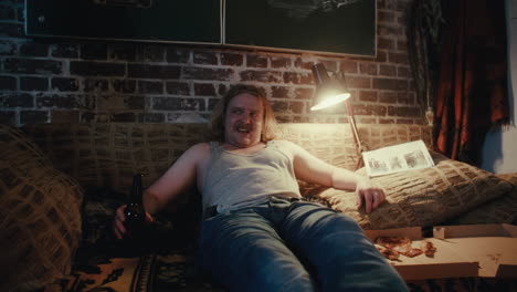 man relaxing on couch with beer and pizza