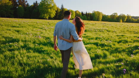 couple walking through a green meadow at sunset
