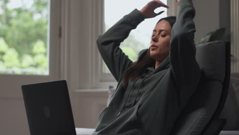 ängstliche frau sitzt zu hause auf einem stuhl, arbeitet von zu hause aus mit laptop und macht sich sorgen um die lebenshaltungskostenkrise