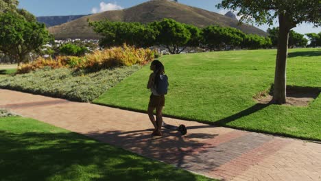 african american woman wearing backpack riding scooter in park