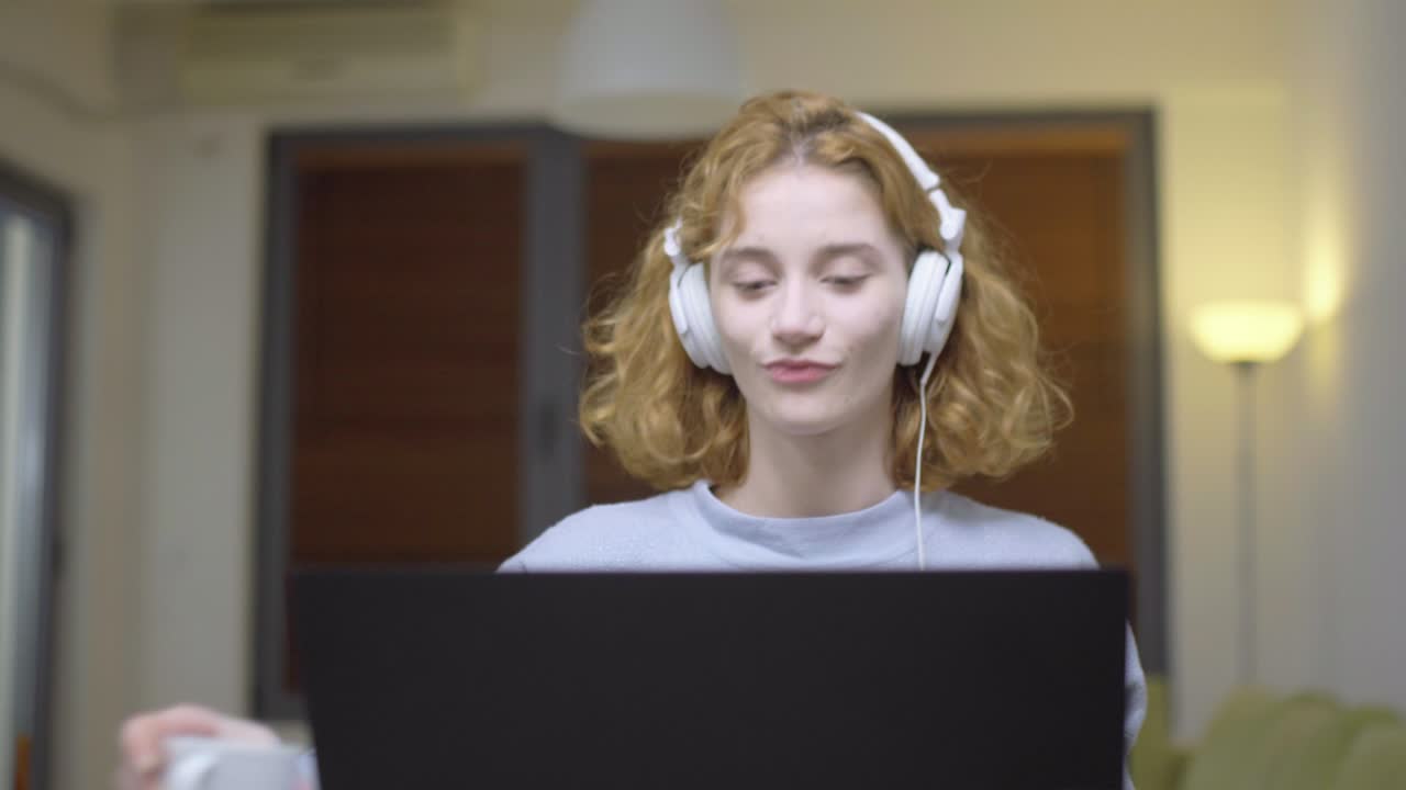 Cute girl sitting on a table in living room infront of a laptop computer. Portrait of a student taking online course. Home education concept.