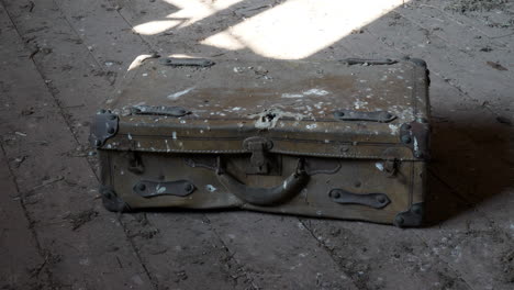 una antigua maleta misteriosa y polvorienta se asienta sobre un suelo de madera en una habitación iluminada por el sol