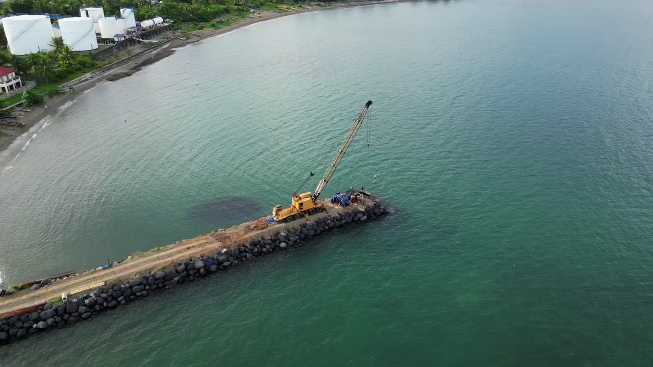órbita aérea de la grúa amarilla estacionada en un rompeolas rocoso en construcción con aguas oceánicas tranquilas en bicol, filipinas