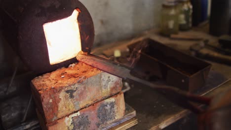 close up hands of caucasian male knife maker in workshop using oven and making knife