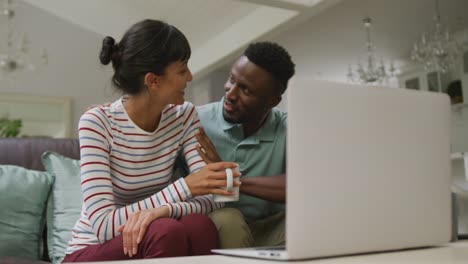 Happy-diverse-couple-sitting-on-couch-and-using-laptop-in-living-room