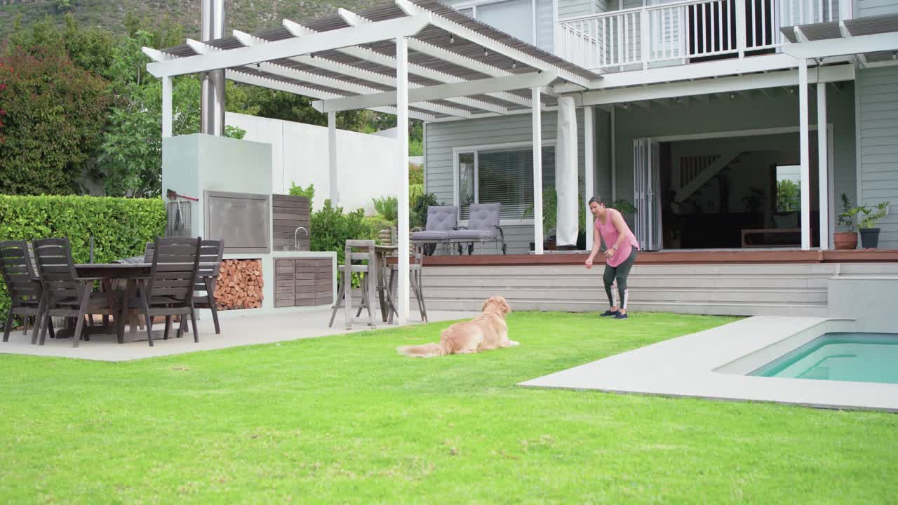Woman is tossing small toy across lawn, after which golden retriever is sprinting to fetch