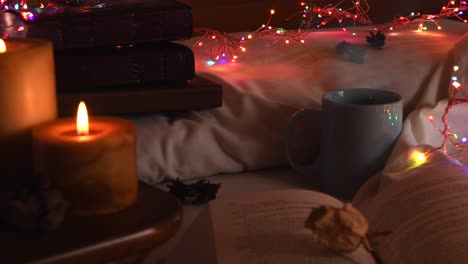 Cozy-background-of-an-open-book-on-a-bed,-next-to-a-mug-and-surrounded-by-colorful-christmas-lights