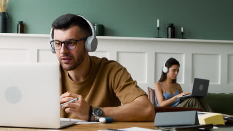 close up view of a student with headphones, using laptop and eating a sandwich sitting at table 1