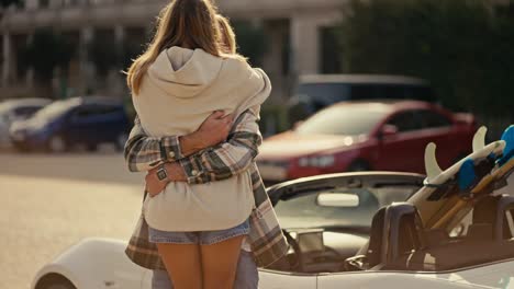 un chico rubio feliz con barba en una camisa a cuadros conoce a su novia rubia en una sudadera blanca, que corre hacia él. una pareja feliz se reúne cerca de un descapotable en un soleado día de verano