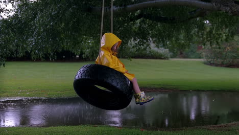 child in yellow raincoat on tire swing by a pond