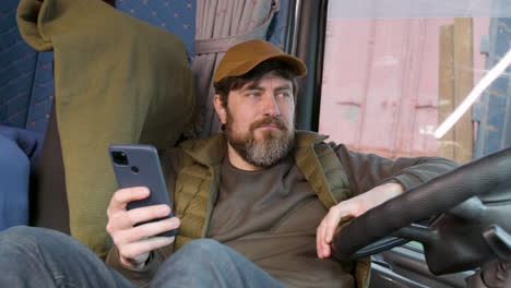Worker Wearing Cap And Vest Tumbado Lying On Truck Seat While Using Smartphone 2
