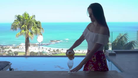 Girl-walking-outside-through-a-door-and-pouring-orange-juice-with-the-ocean-in-the-background