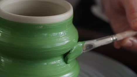 painting a green ceramic pot on a pottery wheel