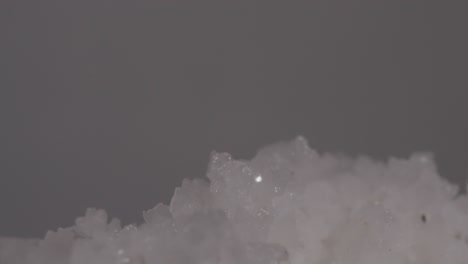 extreme close-up of salt crystals falling onto a mound of coarse white salt grains