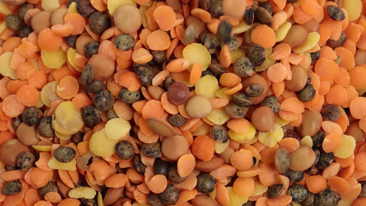 A vibrant mix of lentils and chickpeas cascades onto a surface, captured in slow motion with bright lighting and clear detail