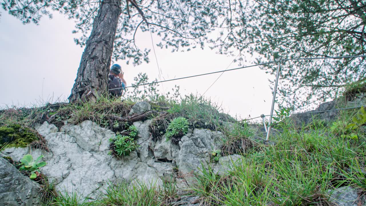 Two hikers reach top of steep rocky trail, raise arms to celebrate. Low angle
