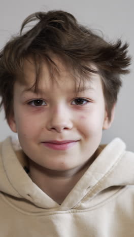smiling brunet boy in a hood looks into camera. teenager takes off his hood and messes his hair. vertical video
