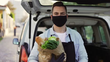 a movement shot of a delivery man wearing protective face mask carrying groceries standing outdoors on the street. coronavirus