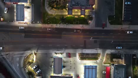 Nighttime-drone-shot-over-commercial-street,-featuring-the-vibrant-lights-of-two-fast-food-restaurants-and-lively-urban-activity